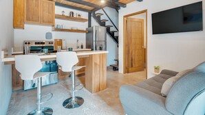 Una cucina compatta con mobili in legno, un frigorifero in acciaio inox e un angolo bar con due sgabelli bianchi.