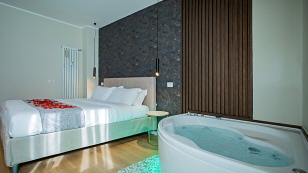 A modern bedroom with a large bed, a small round table, a built-in bathtub, and a decorative wall panel. - Romantic Suite with jacuzzi near Vatican (Room 2) (Roma)