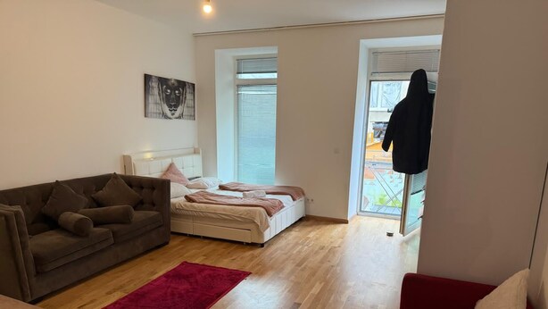 A modern bedroom with a large bed, a sofa, and a red rug. - Comfort 1BR Studio Near Matzleinsdorfer (Vienna)