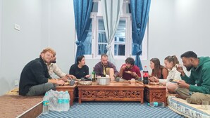 Un grupo de personas sentadas alrededor de una mesa de madera en una habitación con ventana y cortinas.