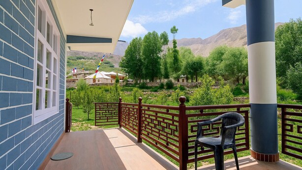 A balcony with a view of a mountainous landscape, a chair, and a building with blue brick walls. - Best place to spend your night in clean and cozy bedroom.
In The Himalaya (Nako)