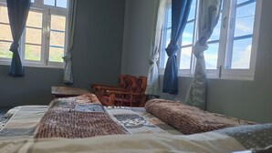 Una habitación con cama, una silla de madera y un ventanal con cortinas.