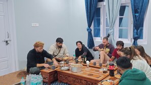 A group of people sitting around a wooden table with food and drinks, in a room with light blue walls and a window with blue curtains. - Best place to spend your night in clean and cozy bedroom.
In The Himalaya (Nako)