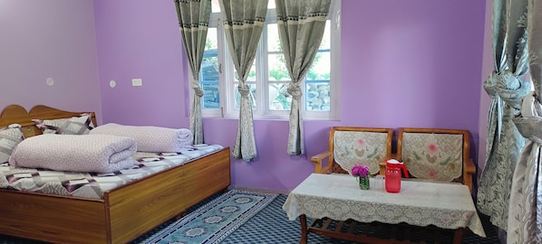 A bedroom with a bed, a table with a vase and a thermos, and a window with curtains.