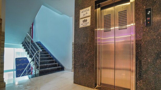 A modern elevator with a sign indicating it is for 3 people only, a stairwell with a blue carpet, and a marble floor. - Sonar Puri Unit 1 (Puri)