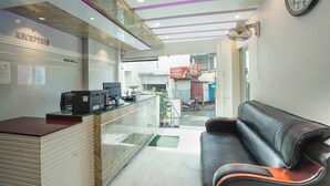 A reception area with a reception desk, a black leather sofa, a clock on the wall, and a ceiling fan. - Sonar Puri Unit 1 (Puri)