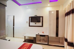 A modern hotel room with a bed, a desk with a chair, a flat-screen TV mounted above the desk, and a wardrobe. - Sonar Puri Unit 1 (Puri)