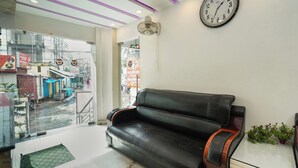 A lobby with a black leather sofa, a wall clock, and a small potted plant. - Sonar Puri Unit 1 (Puri)