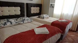 Una habitación de hotel con dos camas, cada una con cabecera, almohada floral y manta roja.