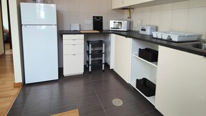 Moderni keittiö, jossa on valkoiset kaapit, sisäänrakennettu mikroaaltouuni, pesuallas ja pieni työtaso.