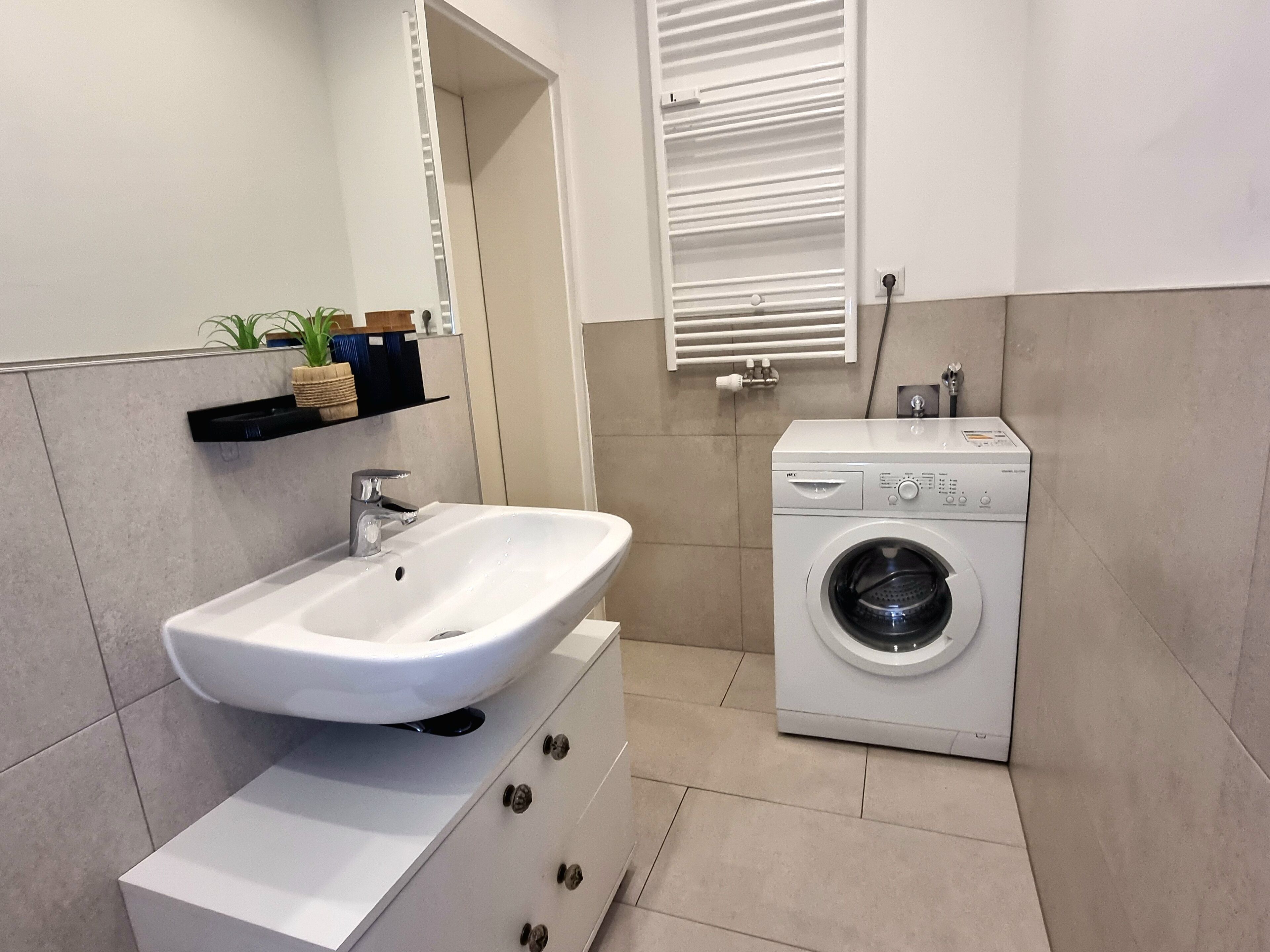 Un baño moderno con un lavamanos blanco, lavadora integrada y un perchero para toallas.