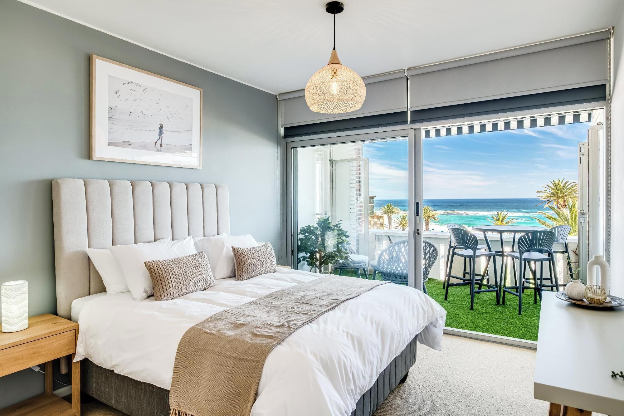 A bedroom with a large bed, a view of the ocean, and a balcony with outdoor seating.