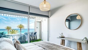 A bedroom with a large bed, a view of the ocean, a balcony with chairs, and a round mirror on the wall. - Camps Bay Seaside Beach View Apartment Palm Bay (Cape Town)