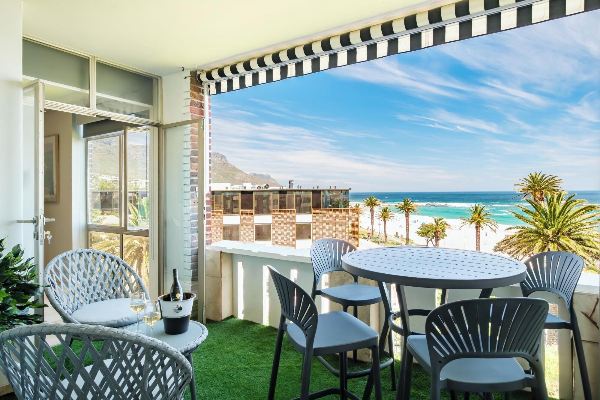 A balcony with a view of the beach, a table with chairs, and a bottle of champagne.
