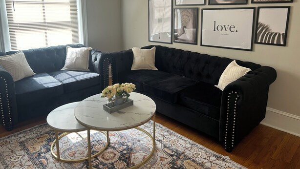 A living room with a black leather sofa, a round coffee table with a vase of flowers, and a patterned rug. - Spacious 2 bedroom with a Deck in center city (Philadelphia)