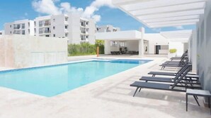 Una piscina amb gandules, una zona coberta i edificis moderns al fons.