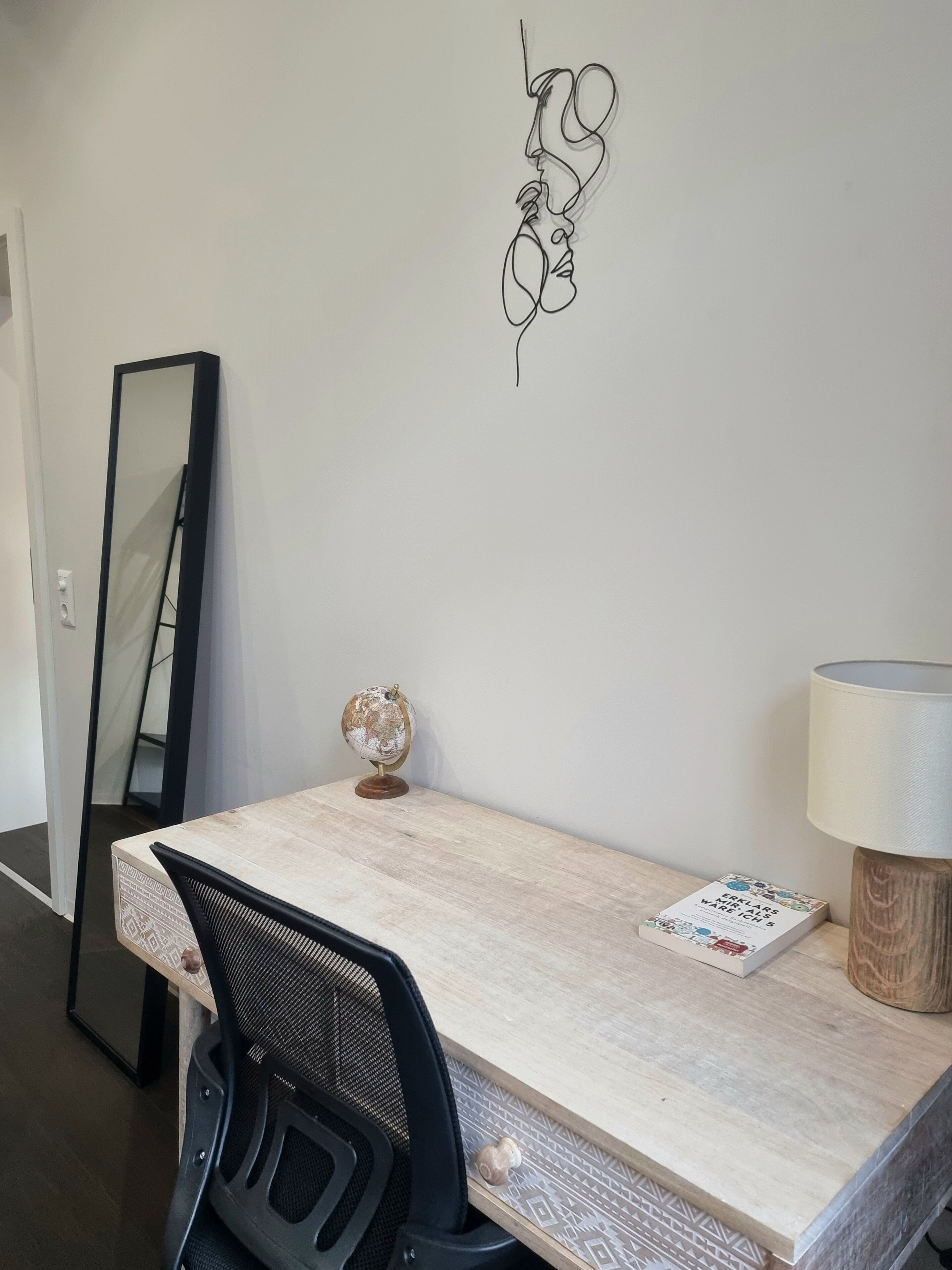 A minimalist office space with a desk, chair, and a wall-mounted mirror.