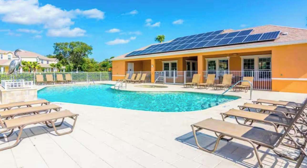 A swimming pool with lounge chairs and a building with solar panels.