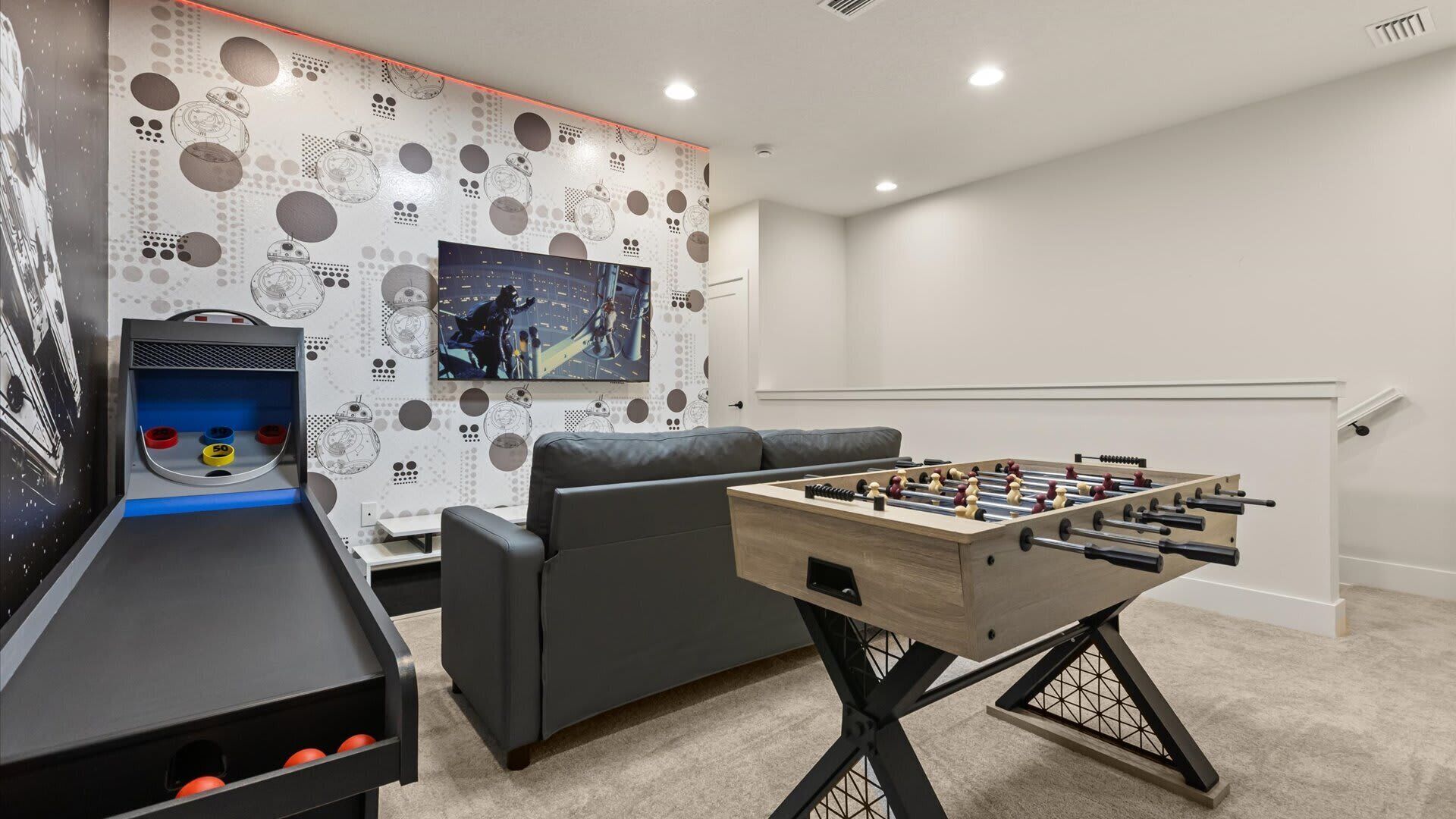 Una habitación acogedora con una mesa de futbolín, un sofá y una pared decorada con motivos de Star Wars.