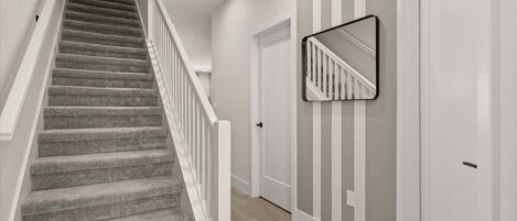 A staircase with carpeted steps and white railings, leading to a door with a striped wall behind it.