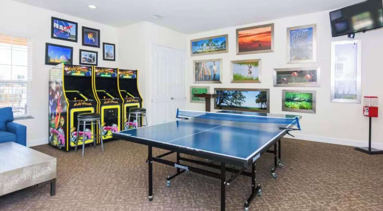 A room with a ping pong table, arcade games, and framed pictures on the walls.