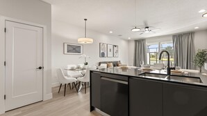 A modern kitchen with a large island, white dining chairs, and a ceiling fan. - Stunning Townhome With Private Pool Games Room (Clermont)
