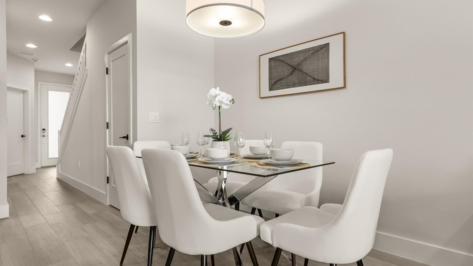 Un espace repas avec une table en verre, des chaises blanches et un luminaire suspendu moderne.
