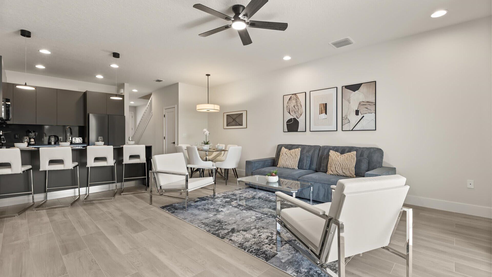 Un salon moderne avec un canapé gris, des chaises blanches, une table basse et un coin repas comprenant une table et des chaises blanches.