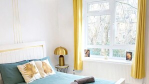 Een slaapkamer met een bed, een bedlampje, een raam met gordijnen en uitzicht op bomen.
