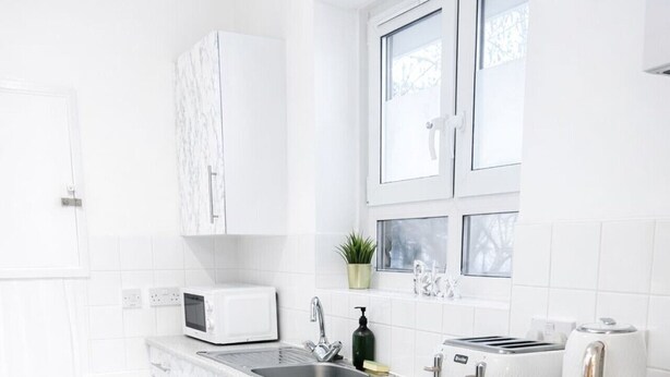 Een moderne keuken met witte marmeren aanrechtbladen, een ingebouwde wasmachine, een broodrooster en een spoelbak.