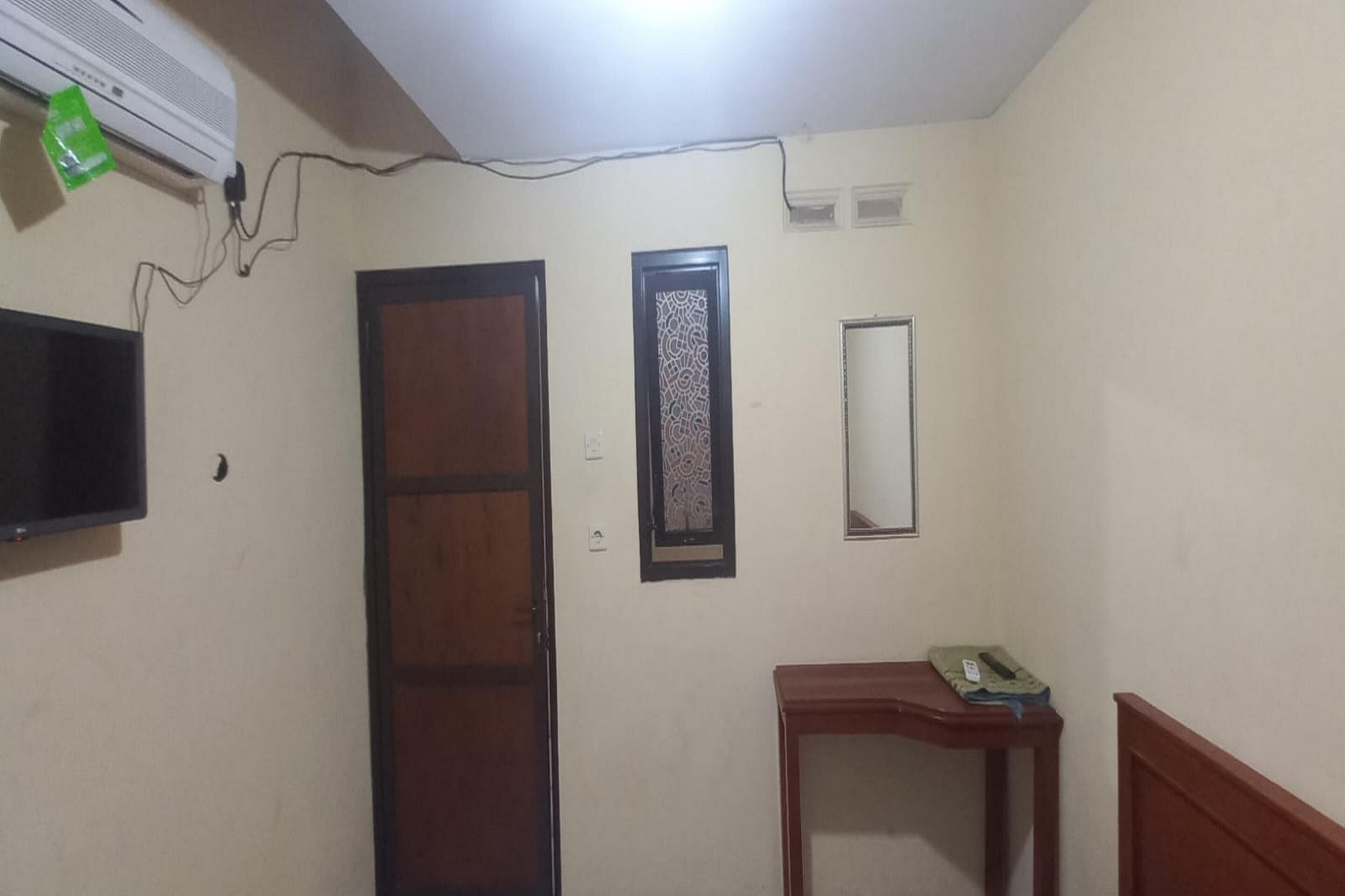 A room with a wooden door, a small table with a telephone, a wall-mounted TV, and a decorative panel.