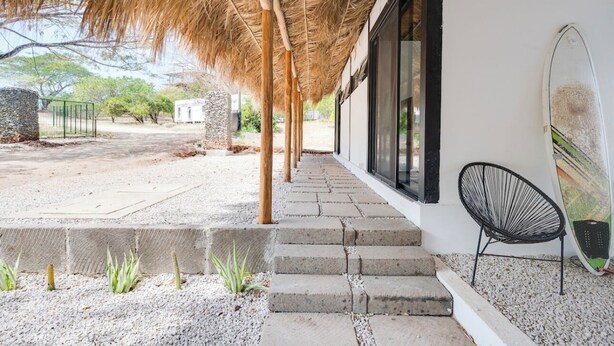 Un espace extérieur abrité, avec un chemin de pierre menant à un bâtiment, une chaise et une planche de surf.