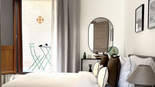 Habitación de hotel con cama, mesita de noche con lámpara, espejo y vistas al exterior.