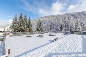 A snow-covered outdoor area with picnic tables and benches, surrounded by snow-laden trees and a mountain backdrop. - Studio Valleverde 21D Ski In Ski Out (Sestriere)