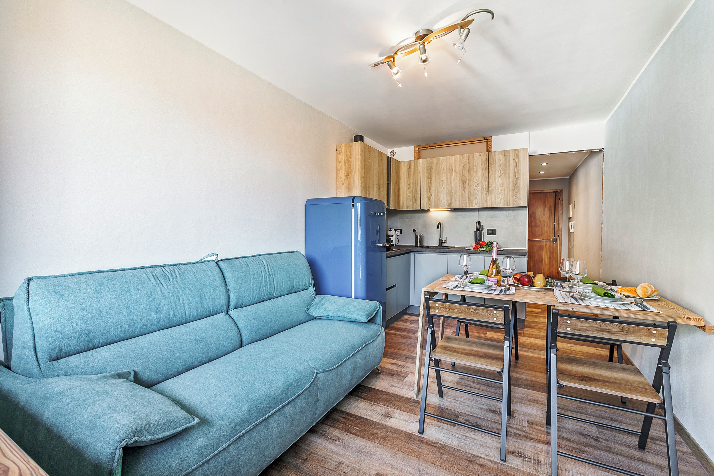 A compact living space with a sofa, dining table, chairs, a refrigerator, and wooden cabinets.