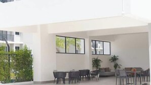 A modern outdoor seating area with tables and chairs, large windows, and a potted plant.