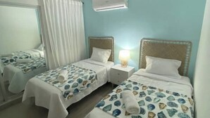 Een hotelkamer met twee bedden, elk voorzien van een bedsprei met een patroon en een wit kussen. Daartussen staat een nachtkastje met een lamp.