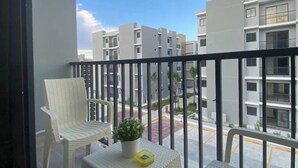 Een balkon met een witte stoel, een tafeltje en een bloempot.
