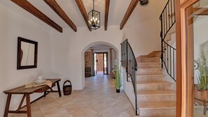 Un hall d’entrée spacieux avec un banc en bois, un escalier doté d’une rampe en fer forgé et un grand miroir accroché au mur.