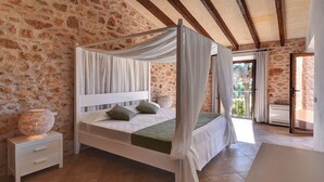Une chambre à coucher avec un lit à baldaquin, des murs en pierre, une table de chevet avec une lampe et une vue sur l’extérieur.