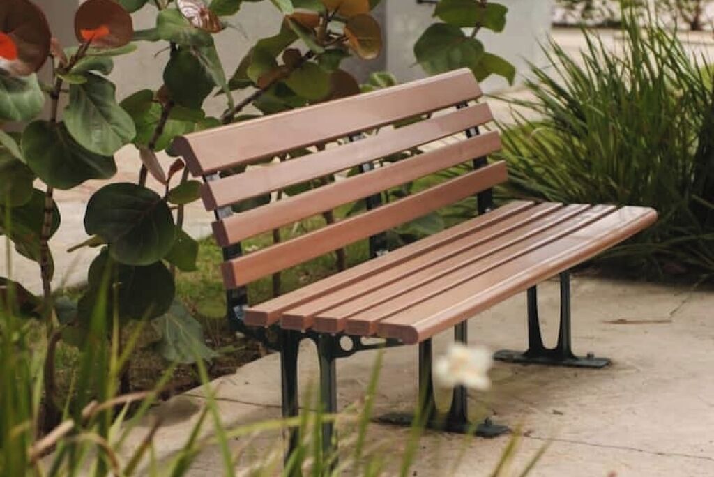 Un banc en bois doté de pieds en métal, placé sur une surface en béton, lui-même entouré de verdure.
