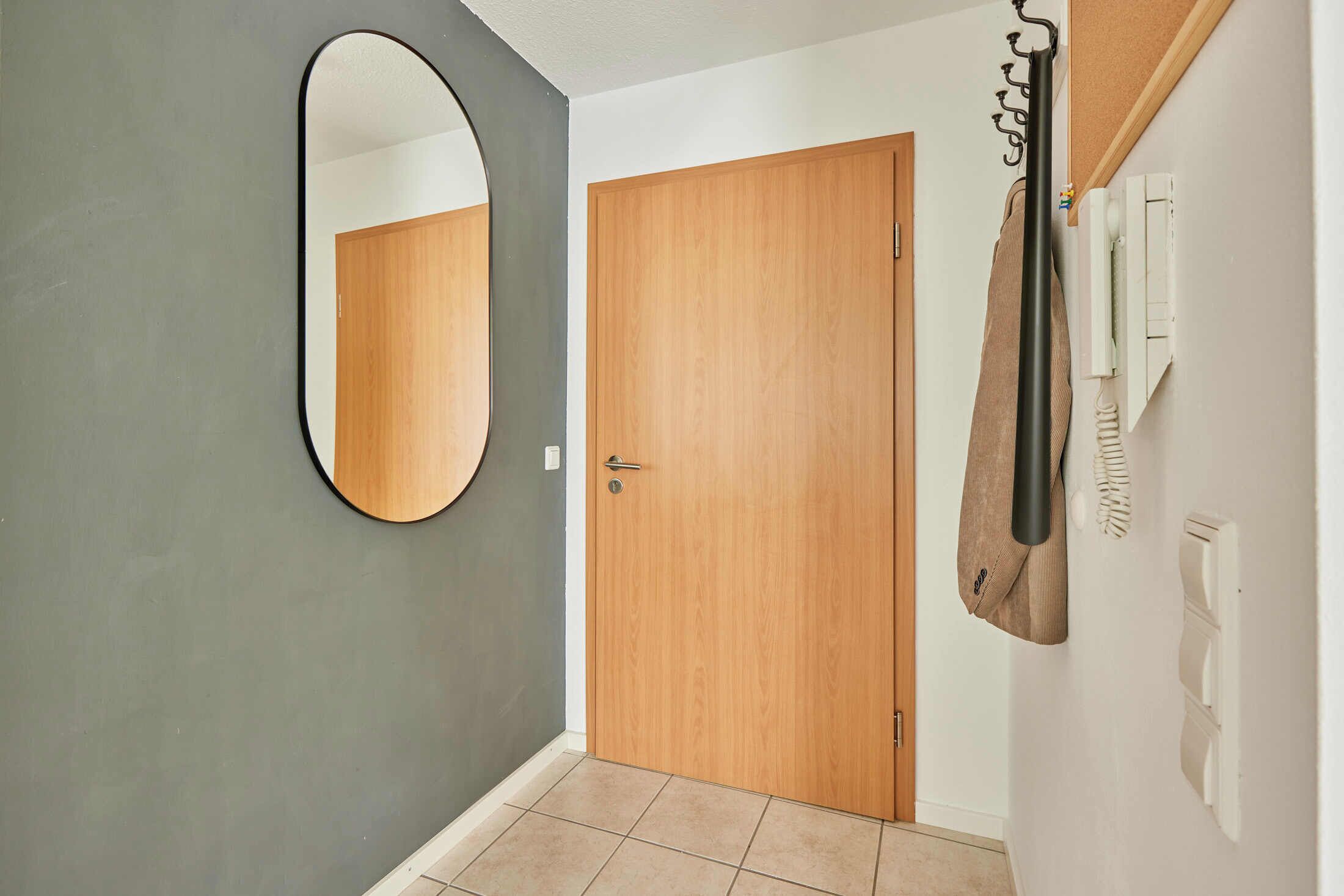 A hallway with a wooden door, a mirror, and a coat rack with a bag.