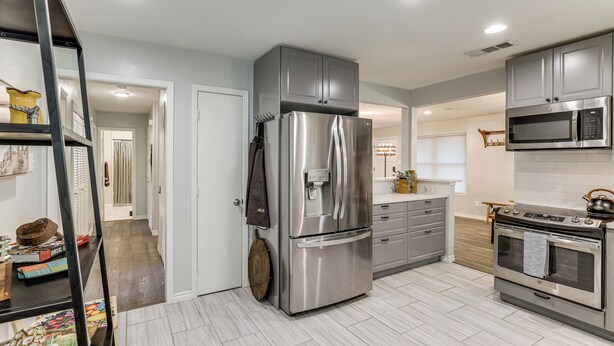 A modern kitchen with stainless steel appliances, grey cabinetry, and a wooden floor. - Dog-friendly Dallas Home w/ Fenced Yard! (Dallas)
