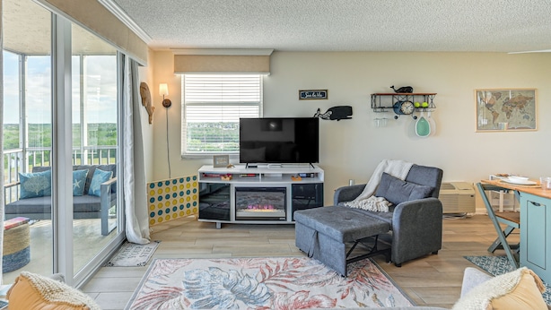 A spacious living room with a large TV, comfortable seating, a fireplace, and a balcony with a view. - Stroll to Bonita Beach Park: Ocean-view Getaway (Bonita Springs)