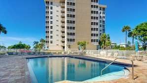 A swimming pool with a tiled deck, surrounded by lounge chairs and a tall building in the background. - Stroll to Bonita Beach Park: Ocean-view Getaway (Bonita Springs)