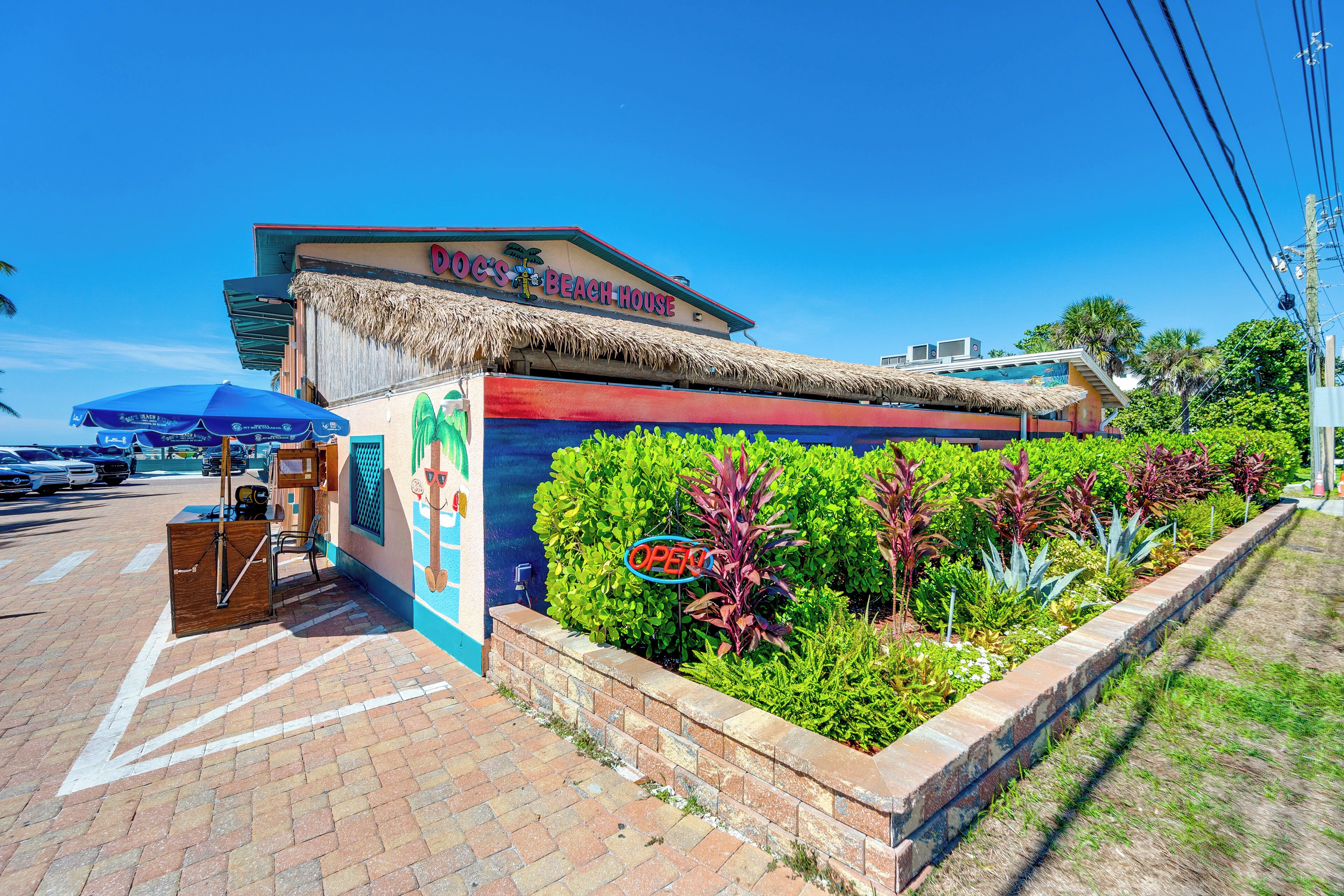 A beach-themed restaurant with a thatched roof, outdoor seating, and a sign indicating it is open.