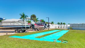 A grassy area with a blue tarp, a trailer, and a boat. - Stroll to Bonita Beach Park: Ocean-view Getaway (Bonita Springs)