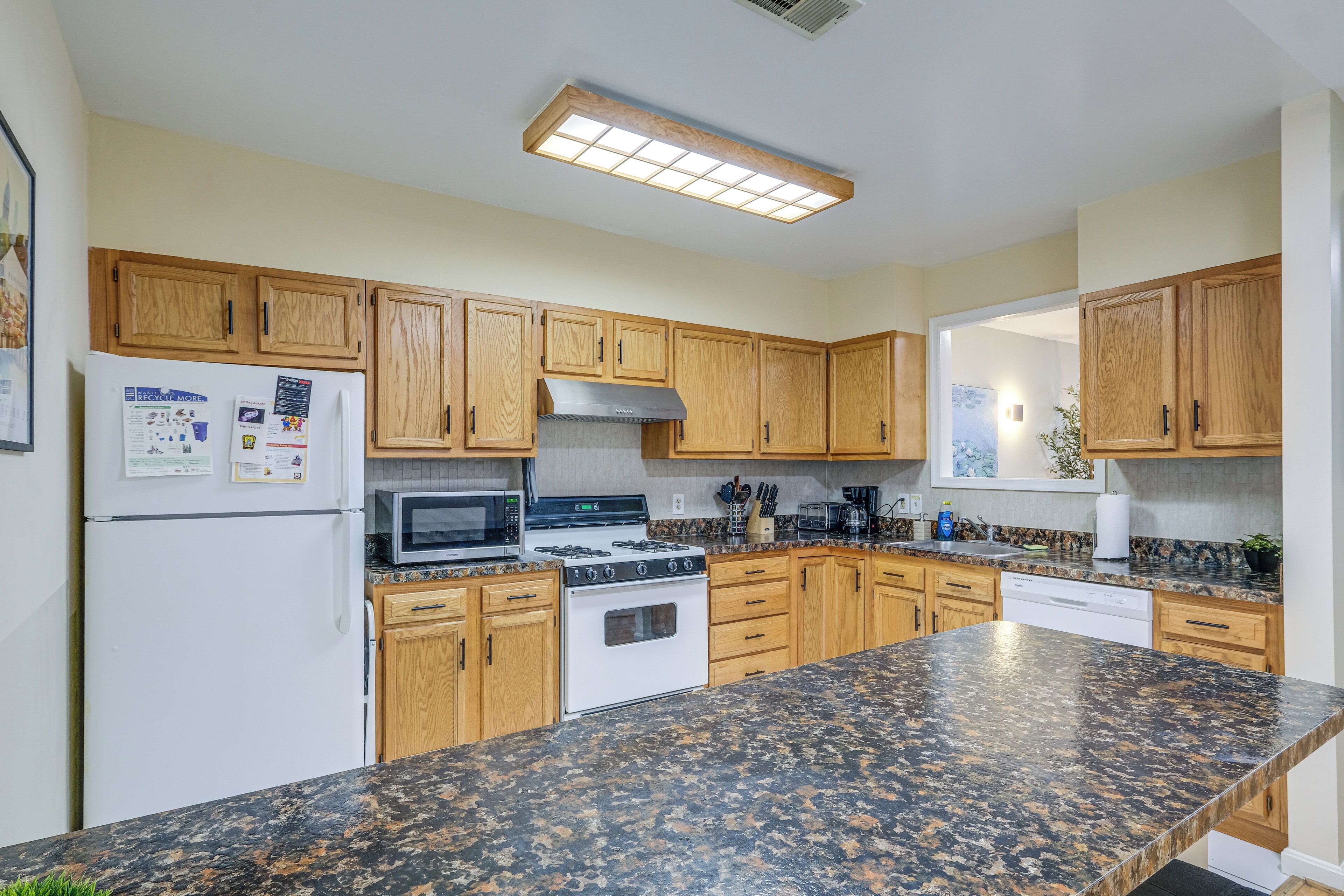 A kitchen with wooden cabinets, a white refrigerator, a microwave, a stove, and granite countertops.
