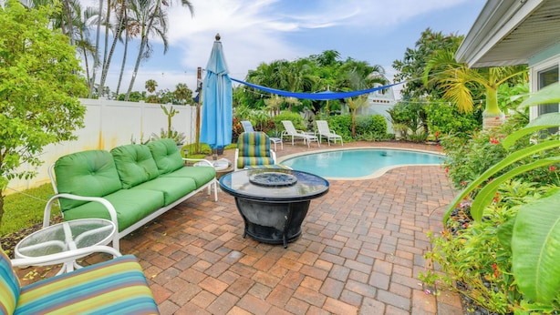A backyard with a swimming pool, a green sofa, white chairs, and a table. - Private Hot Tub, Pool & Yard: Modern Bradenton Gem (Bradenton)