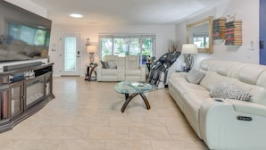 A spacious living room with a large flat-screen TV, a glass coffee table, a white leather sofa, and a beige tiled floor. - Private Hot Tub, Pool & Yard: Modern Bradenton Gem (Bradenton)